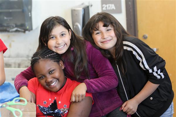 three upper elementary students hug in a classroom 